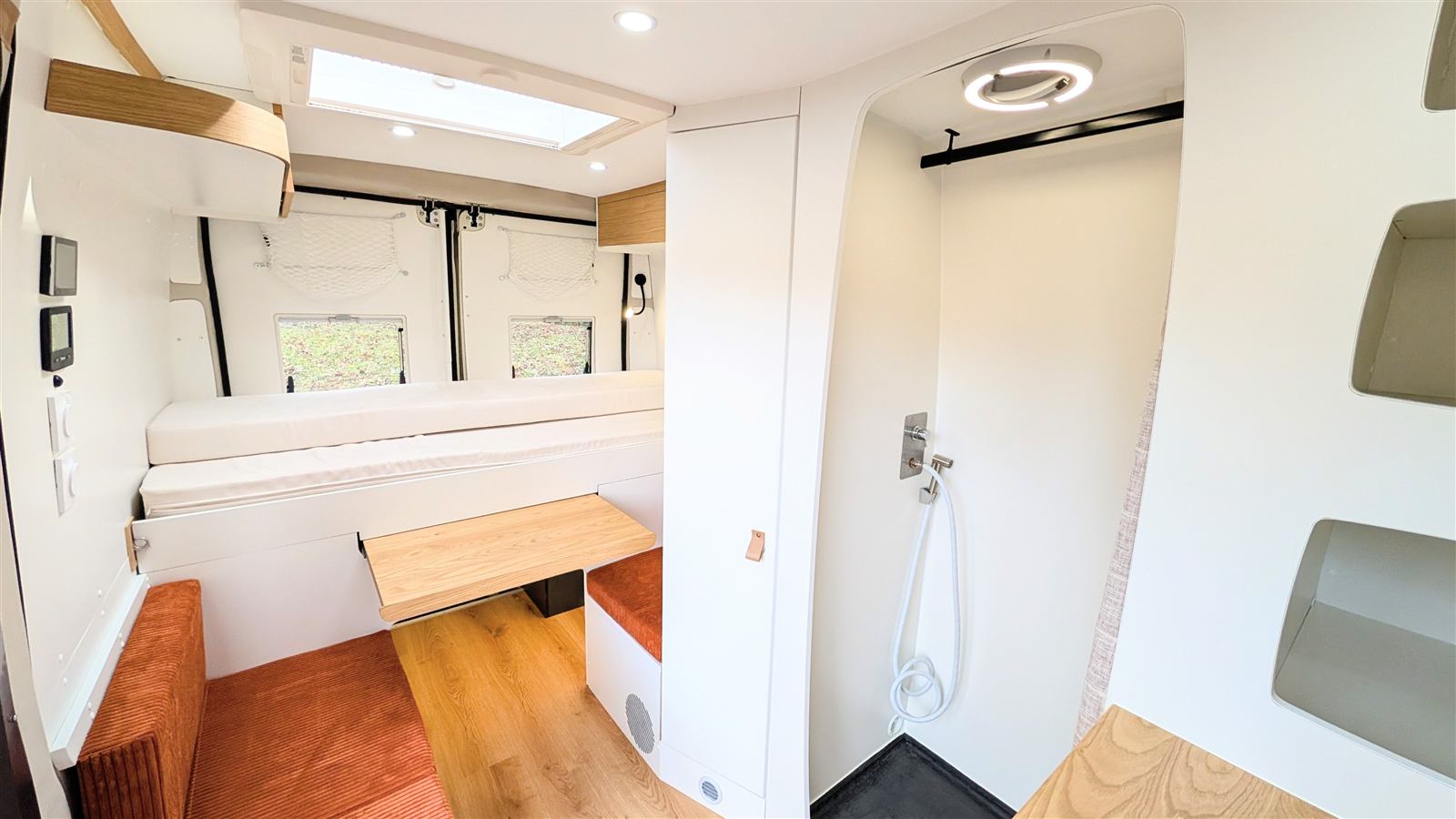 Intérieur de van aménagé : cabine de douche, couchage et table escamotable